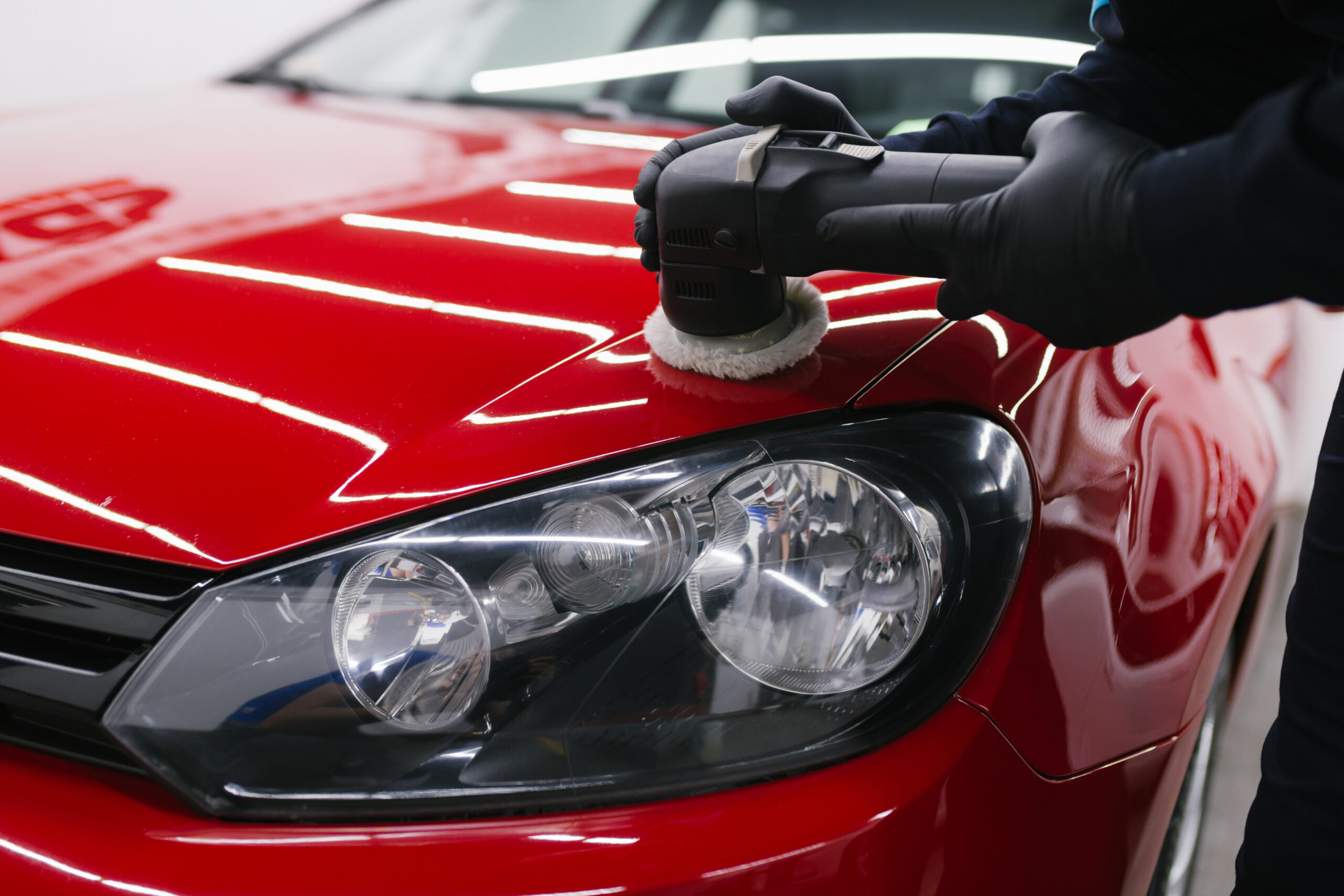 Car detailing - Man with orbital polisher in repair shop polishing car. Selective focus.