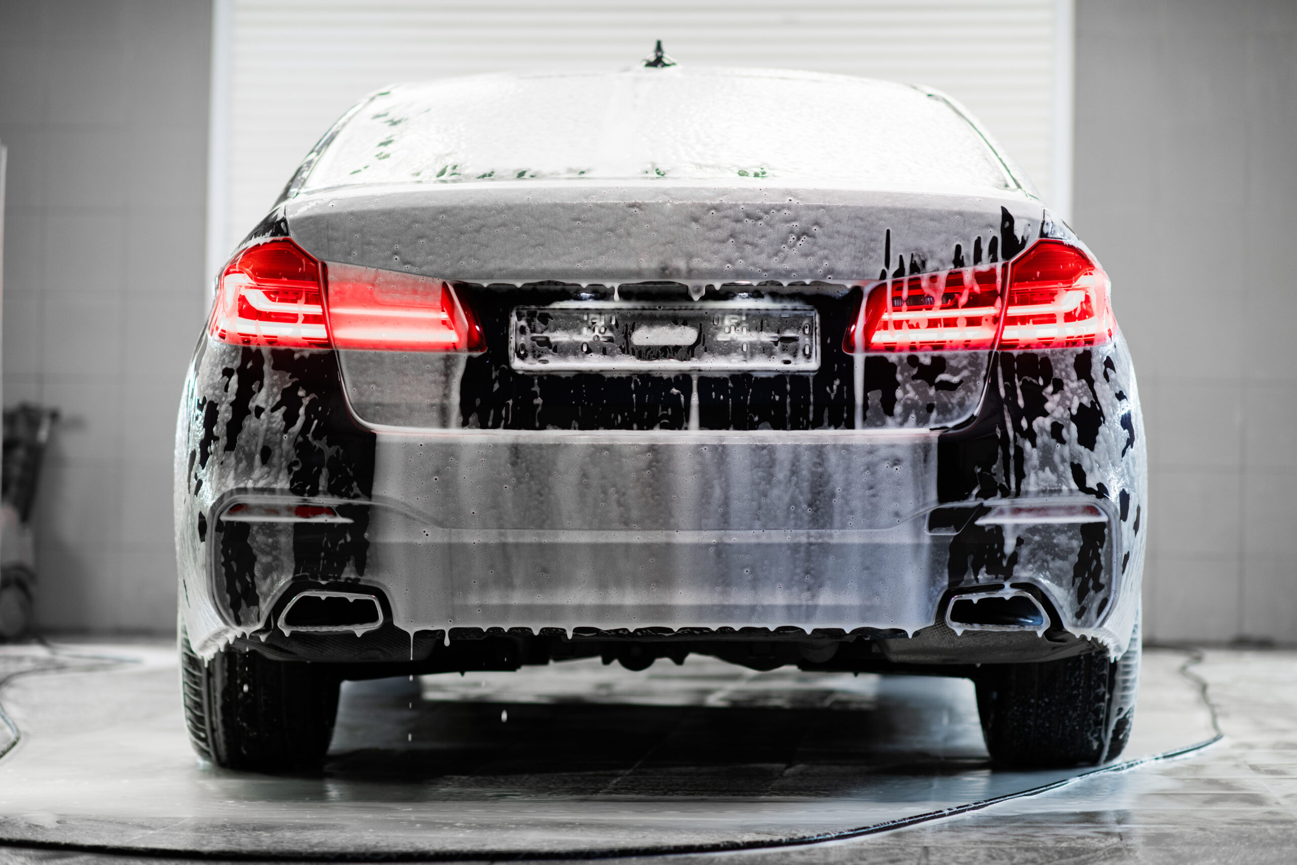 Car with turned on backlights standing in car wash service covered with a foam